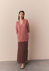 Rožinės spalvos megztinis su apykakle ir V formos iškirpte, derinamas su ilgu burgundiško atspalvio sijonu ir minimalistinėmis auksinėmis sandalais.