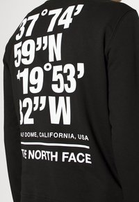 Svart sweatshirt med fet vit text som visar geografiska koordinater och "HALF DOME, CALIFORNIA, USA" längst ner.