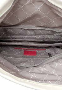 Interior de bolsa blanca con forro gris que presenta un patrón de puntos. Incluye una etiqueta de acento roja y múltiples compartimentos para la organización.