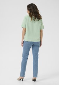 Top corto verde menta a maniche corte con tessuto testurizzato, con un nodo al collo, indossato con jeans blu chiaro e tacchi beige.