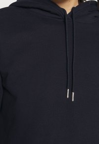 Sudadera con capucha de algodón en azul marino oscuro, con capucha ajustable con puntas de metal plateadas, textura suave y un corte relajado.