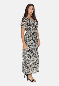 Robe maxi en tissu léger, avec une base noire ornée de motifs floraux blancs et jaunes, taille cintrée et manches courtes bouffantes.