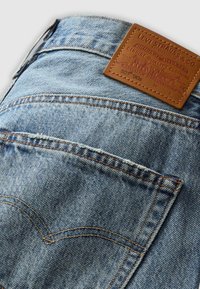 Lichtblauwe denim jeans hebben een bruine leren label op de taille met gegraveerde merkdetails, zichtbare naden en een klassiek zakontwerp.