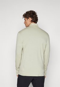 Light green long-sleeve shirt with a high collar, featuring a smooth texture and a relaxed fit. Minimalist design, no visible patterns or accents.