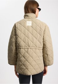 Beige gesteppte Jacke mit hohem Kragen und einem Logo-Patch. Verfügt über weite Ärmel und ein tailliertes Einsatz für eine lässige Passform.
