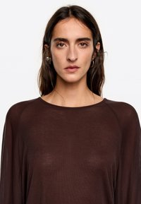 Bruine lange mouwen top met een relaxte pasvorm en zachte textuur. Heeft een ronde halslijn en subtiele details op de schouders.