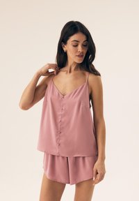 Pink satin camisole with thin straps, v-neck, front buttons, and two pockets; paired with matching pink shorts. Smooth texture, relaxed fit.