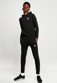 Conjunto de sudadera con capucha y pantalones de chándal de tela suave. Presenta un bolsillo tipo canguro, puños ajustados y acentos de logo blanco en ambas piezas.