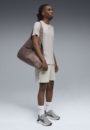 Grijs T-shirt met logo, lichtgekleurde shorts en grijze sneakers met zwarte accenten. Bruine schoudertas met een ritsvak.