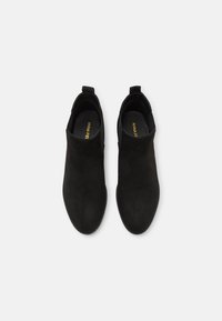 Black ankle boots made of suede, featuring a smooth texture and a sleek, tapered design with pull tabs on the back. No visible hardware.