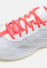 Light gray athletic shoe with textured upper, red laces, and silver accents. Features mesh fabric and reinforced eyelets for support.