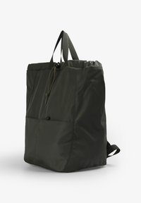 Mochila de nylon verde oscuro con cierre de cordón, bolsillo frontal, dos asas superiores y correas ajustables para mayor versatilidad.
