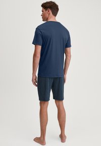 Marineblauwe T-shirt met een ronde hals, gecombineerd met gestreepte marineblauwe shorts met een gestructureerd ontwerp. Model staat blootsvoets en toont de achterkant.