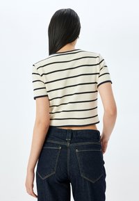Top corto a maniche corte color crema con strisce nere. Presenta un tessuto a maglia texturizzato e un collo a costine. Abbinato a jeans a vita alta blu scuro.