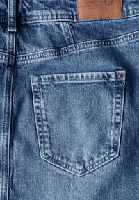 Světlé modré džínové kalhoty s kapsou vzadu s prošitým obrysem a koženou štítkem na pásku. Hladká textura.