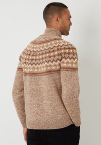 Beige pletený svetr s vysokým límcem, s vzorovaným sedlem v oranžové a hnědé barvě a strukturovaným tělem. Žebrovaný lem a manžety.
