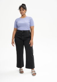 Lichtpaarse geribde t-shirt met korte mouwen, gecombineerd met hoge zwarte wijde jeans en grijze sandalen met verstelbare banden.