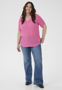 Haut rose à manches courtes avec encolure en V et coupe décontractée, associé à un jean bleu évasé et des chaussures noires. Texture unie, design casual.