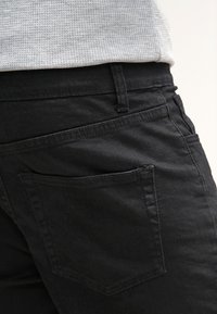 Jeans de mezclilla negra con una textura suave, que cuentan con un bolsillo trasero y costuras sutiles. La cinturilla presenta un diseño de bucle sencillo.
