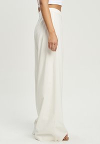 Spodnie o szerokich nogawkach w jasnym beżowym kolorze z gładkiego materiału. Charakteryzują się wysokim stanem i luźnym krojem, oferując swobodny fason.