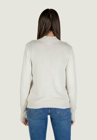 Kremowy sweter z dzianiny z prążkowanymi mankietami i hemem, z wysokim kołnierzem. Noszony z niebieskimi dżinsami w slim fit.