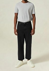 Černé džíny s širokými nohavicemi, vyrobené z denimu, s pěti kapsami, zapínáním na knoflíky a hladkým povrchem. Kombinované s šedým tričkem s krátkým rukávem.