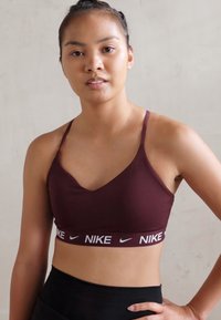 Bordó sportmelltartó V-nyakú fazonnal, vékony pántokkal és egy fehér Nike logós szalaggal az alján. Simább, elasztikus anyag.