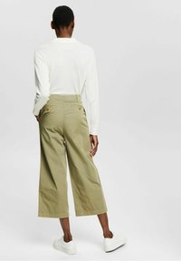 Cropped, wide-legged trousers in olive green cotton with two back pockets. Paired with a white long-sleeve top and white sneakers.
