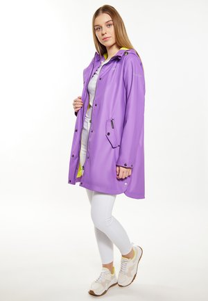 Cappotto impermeabile viola con cappuccio, con zip frontale, tasche a pressione e dettagli gialli. Abbinato a leggins bianchi e scarpe sportive.