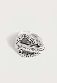 Ασημένιο δαχτυλίδι Ed Hardy με χαραγμένο το όνομα της μάρκας σε διακοσμητική υφή οβάλ επιφάνεια, σε λευκό φόντο.