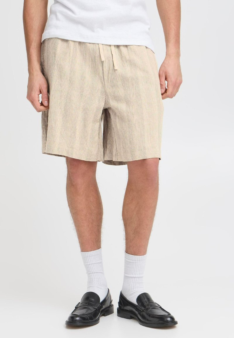 Shorts rayés beige avec une taille élastique et un cordon de serrage. Le tissu a une apparence texturée et tombe juste au-dessus du genou.