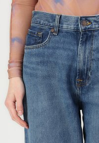 Høyt livdede blå denim jeans har et rett ben-design, subtil falming, oransje sømdetaljer og en frontlomme.