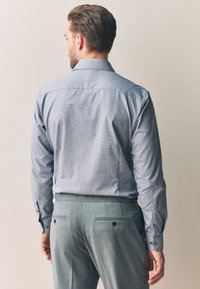 Kék kockás ing hosszú ujjakkal, gombos mandzsettákkal és hátpánttal, világosszürke nadrággal párosítva, amely oldalsó és hátsó zsebekkel rendelkezik.