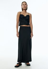Zwart satijnen twee-delige set met een cropped top met een cowln neckline en een vloerlange rok, beide met een gladde textuur en een minimalistisch ontwerp.
