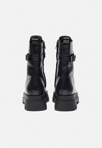 Bottes noires en cuir à chevilles avec une finition lisse, une semelle épaisse, des fermetures éclair et des sangles ajustables au niveau des chevilles pour un maintien sécurisé.