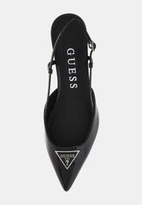 Black patent leather pointed-toe slingback with a triangular silver GUESS logo and a thin ankle strap. Smooth texture and sleek design.