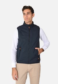 Gilet senza maniche blu navy realizzato in tessuto liscio, con colletto alto, apertura con zip e tirazip arancioni, dotato di tasche laterali.