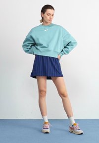Fénykék cropped pulóver fehér logóval, tengerészkék csíkos szoknyával párosítva. Fehér zoknik és színes tornacipők egészítik ki a megjelenést.