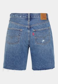 Jeansshorts i ljusblått med fransar i fållkanten, två bakfickor, gul söm och en brun läderlapp i midjan.