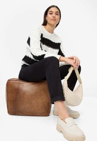 Strikket sweater med hvide og sorte striber, kombineret med sorte bukser. Modellen har beige chunky loafers på og bærer en lys beige skuldertaske.