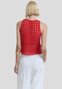 Red crochet halter top with openwork design, scalloped hem, and a keyhole closure at the back, paired with white wide-leg pants.