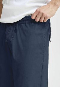 Navy blue shorts made of lightweight fabric with an elastic waistband, drawstring, and side pocket. Smooth texture with minimal stitching.