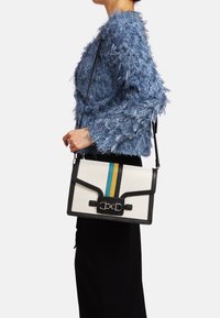 Borsa strutturata con corpo in tela bianca, dettagli neri e strisce verticali verdi, gialle e blu. Presenta una chiusura con gancio in metallo.