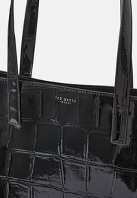  saco de mão preto em verniz com padrão de crocodilo, apresentando duas alças e uma placa de logo em dourado estampada na parte frontal.