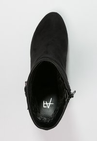 Bota de tobillo de ante negro con cremallera lateral, vista desde arriba, mostrando el logotipo de la marca en el interior.