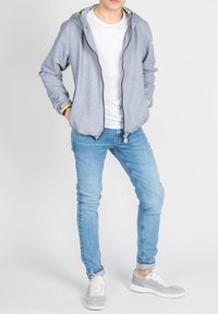 Lys grå zip-up hoodie med gule detaljer, parret med en hvid T-shirt og lyseblå skinny jeans. Hvide og grå sneakers.