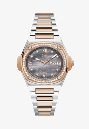 Rózsaarany és ezüst fém óra nyolcszögletű tokjával, szürke gyöngyház számlappal, gyémánt díszítéssel és dátumkijelzővel. Ezüst szíj láncszemek.