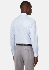 Camisa de rayas azul claro de manga larga, vista por detrás. Combinada con pantalones de traje gris claro, con dos bolsillos traseros y un cinturón negro.