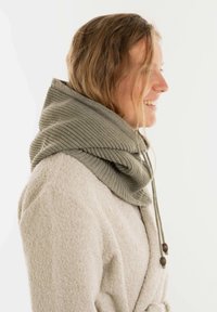 Gebreide groene fleece sjaal met ribbeltextuur, voorzien van een trekkoordsluiting met houten knoppen, gedragen over een lichtbeige badjas.
