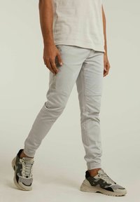 Pantalon gris clair évasé en tissu mélange de coton, présentant des détails de couture minimaux et une coupe slim. Associé à des baskets multicolores.